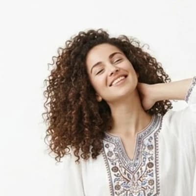 A woman with curly hair laughing, photographed against a plain white backdrop.