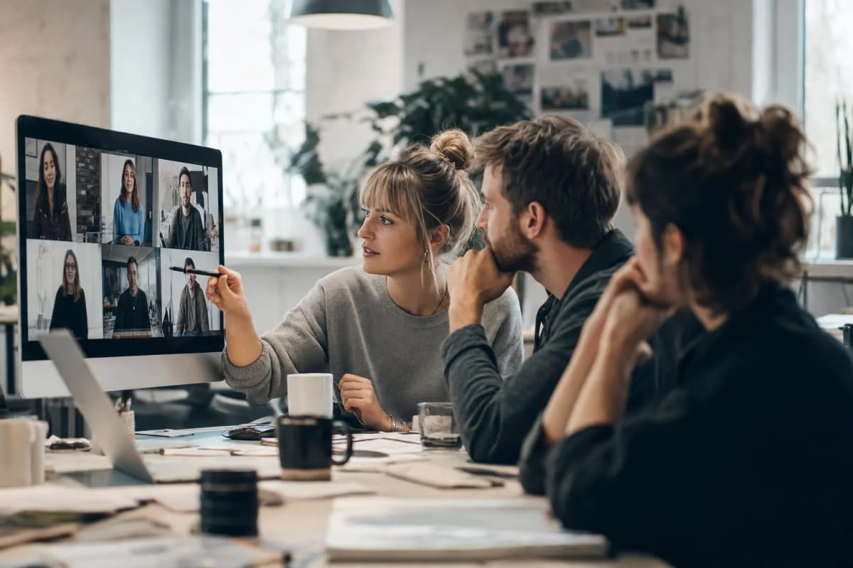 Three colleagues review a grid of presenter videos together on one monitor.